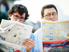 A young and older man looking through the jobs ads section of a newspaper