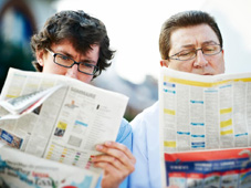 Junger und älterer Mann betrachten gemeinsam die Stellenangebote in einer Zeitung