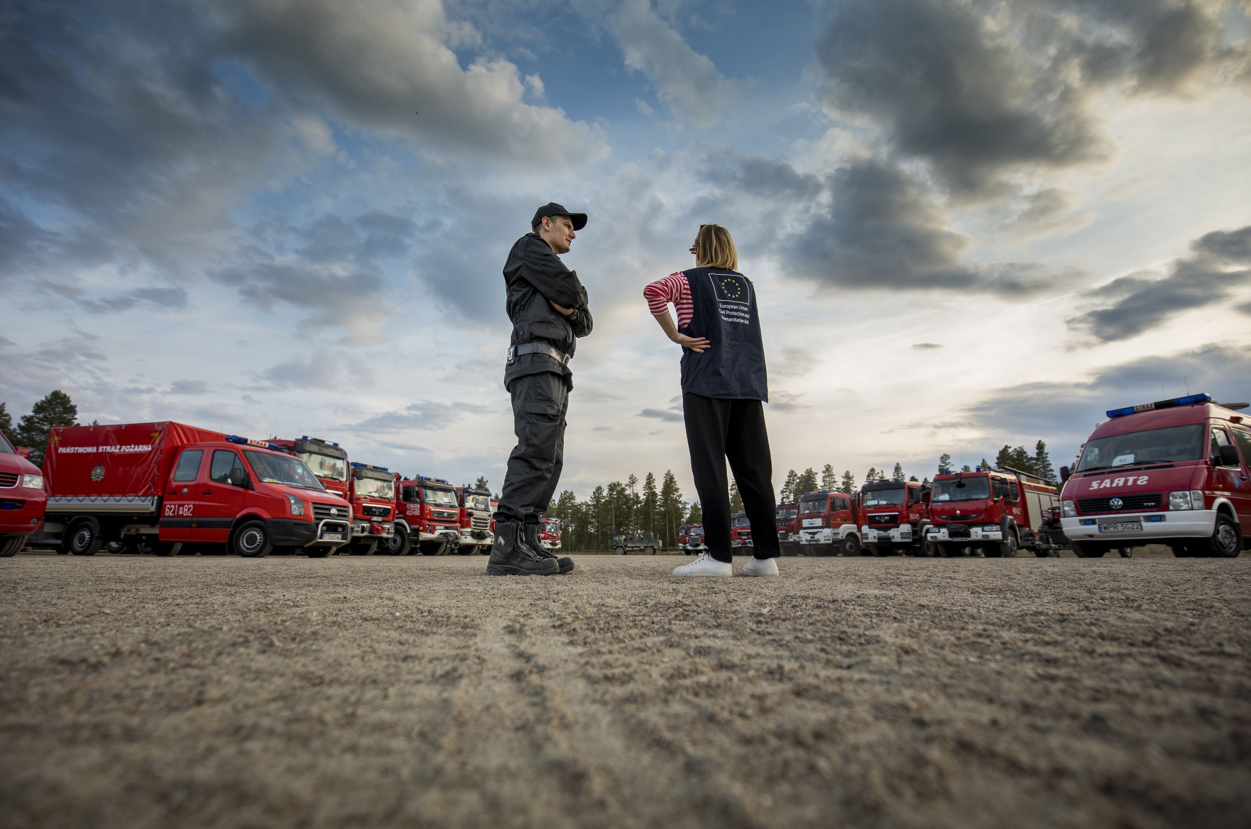 Two people stand in front of fireservice vehicles.