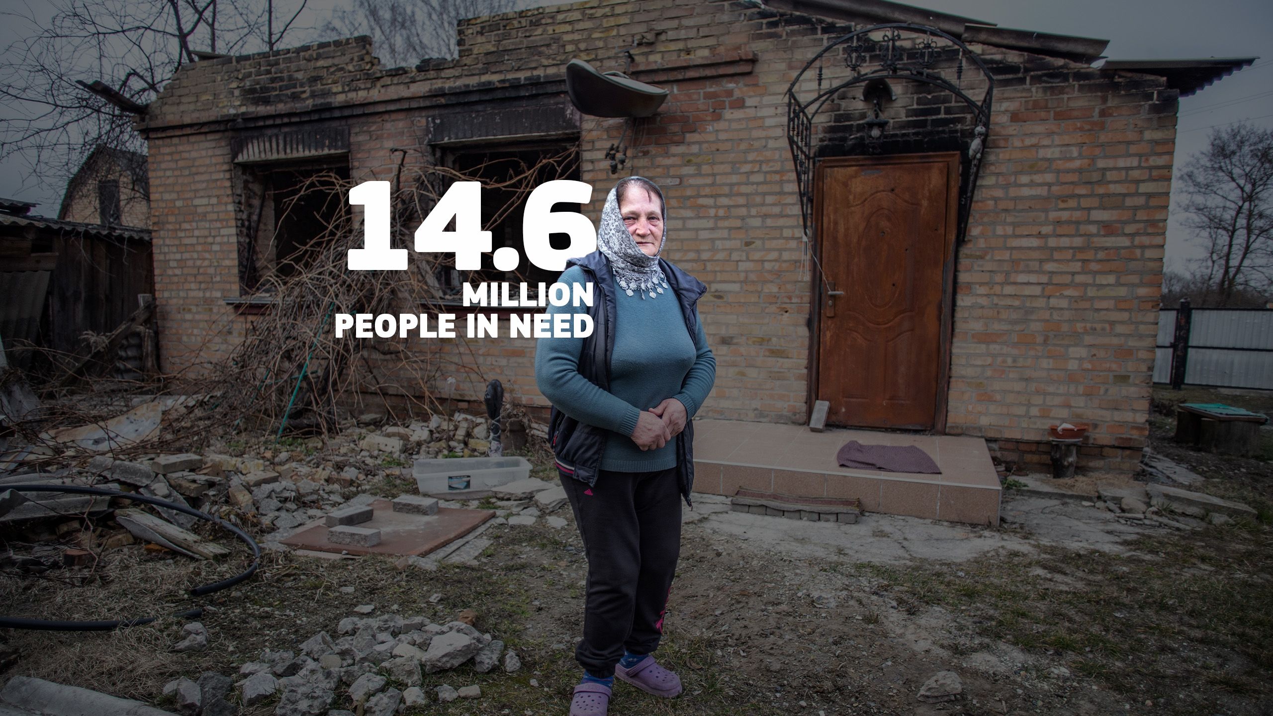 A woman stands in front of her destroyed house.